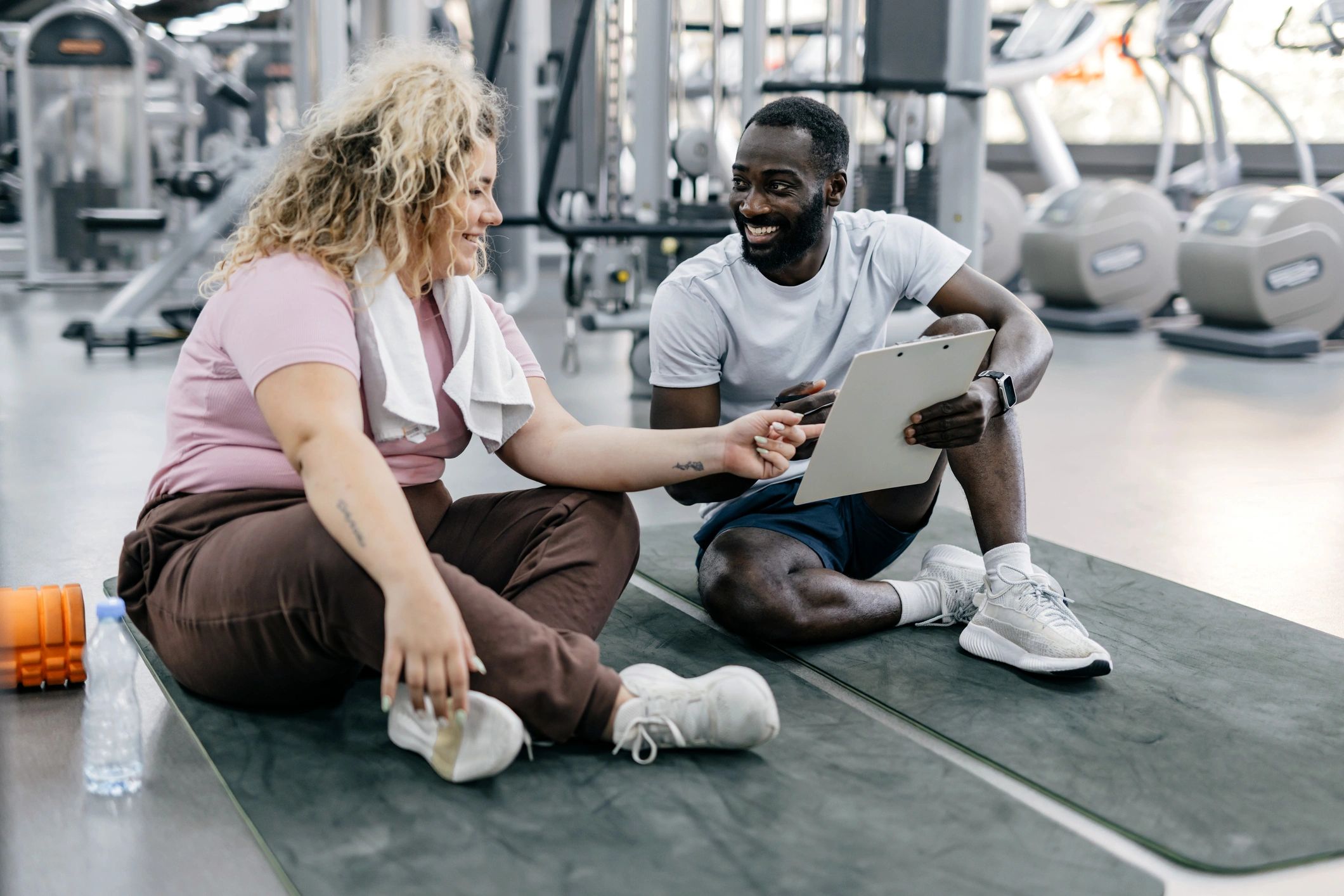 Trainer and client reviewing a workout plan on mats in the gym